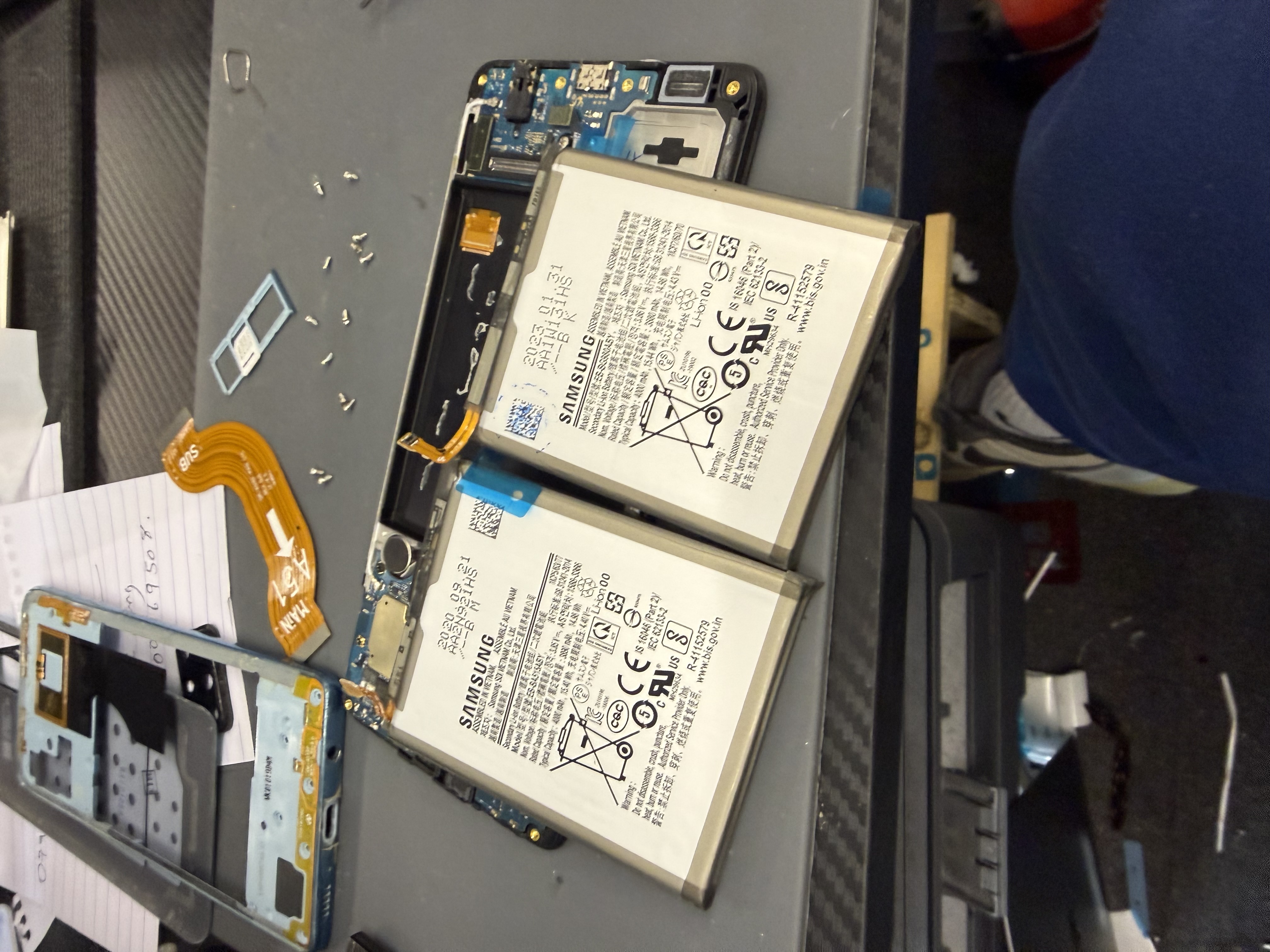 Samsung phone chassis with original and replacement batteries during a battery swap